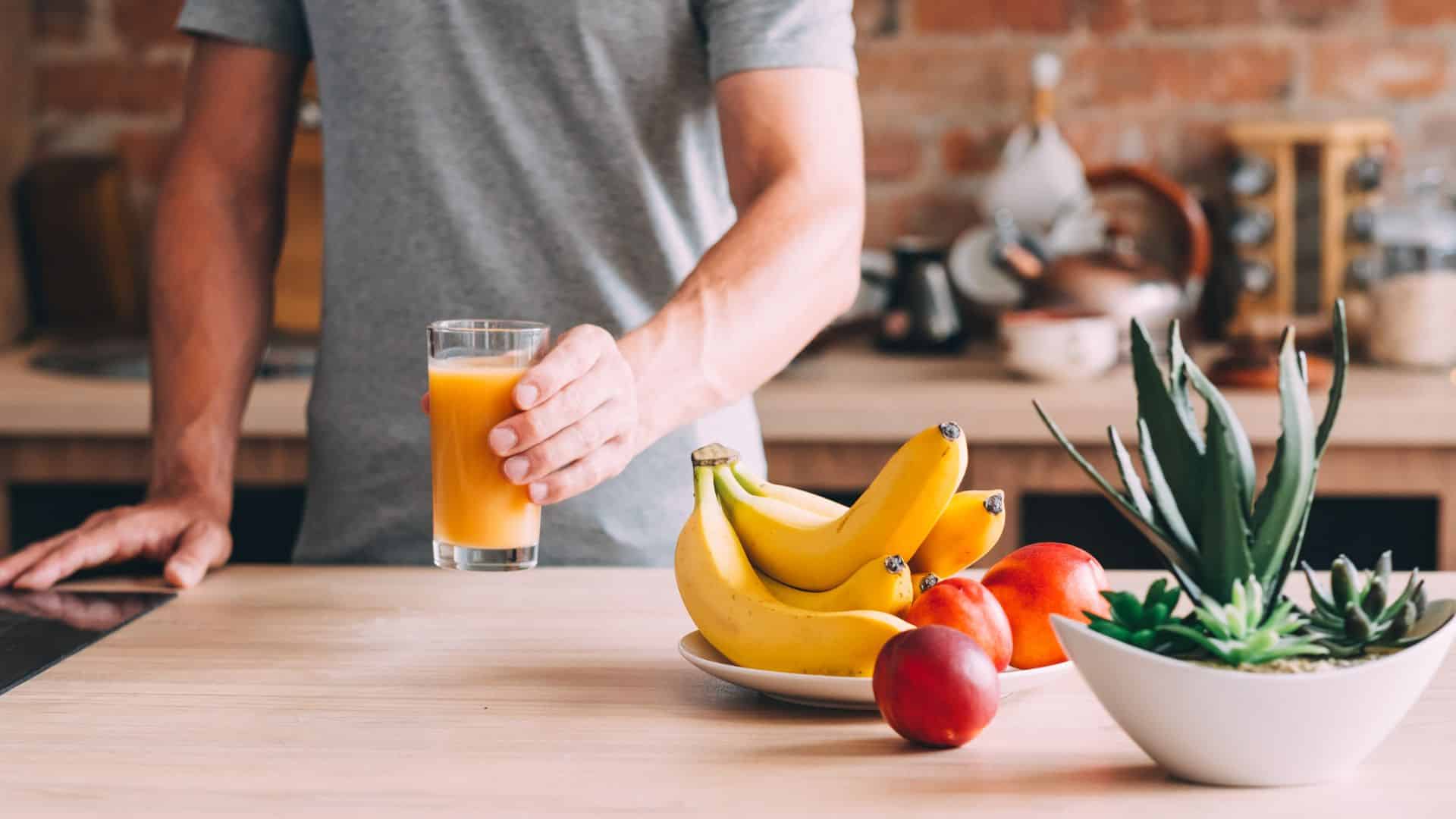 Mann mit Saftglas und frischem Obst auf dem Tisch