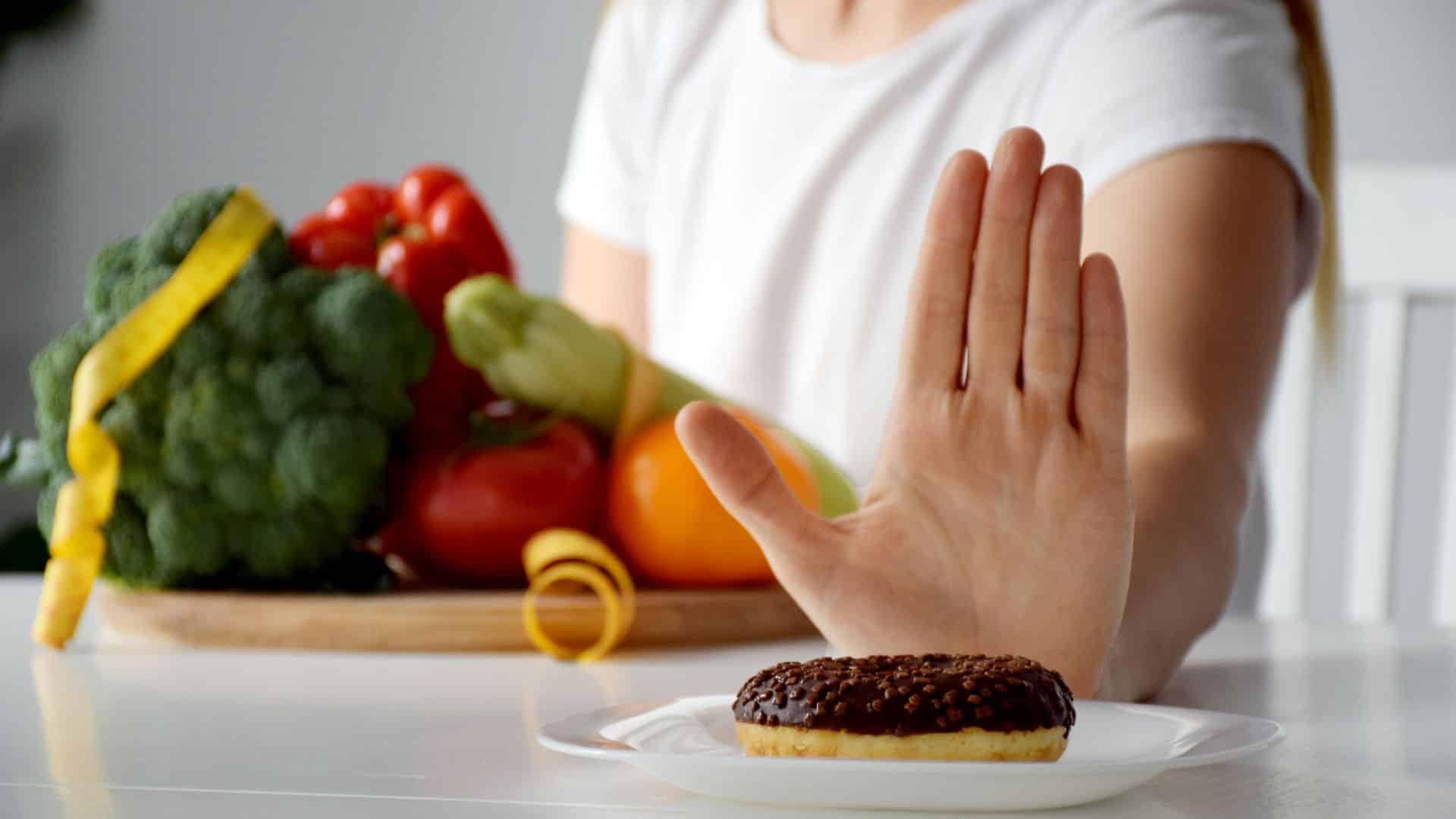 Frau, die Donut wegschiebt und Gemüse in der anderen Hand hält